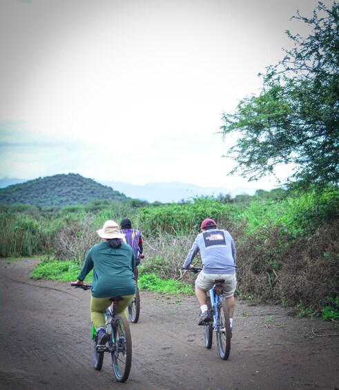 Three cyclists on a dirt path with greenery and hills in the background. 2
