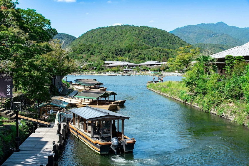 A river with boats docked at a wooden pier, surrounded by lush greenery and mountains in the background. 1