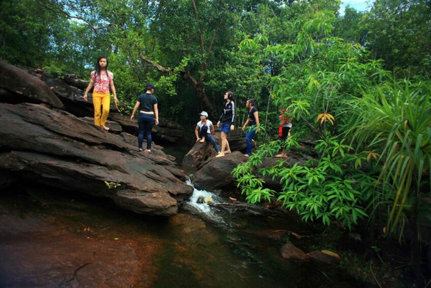 People walking on rocks by a stream in a forest. 4
