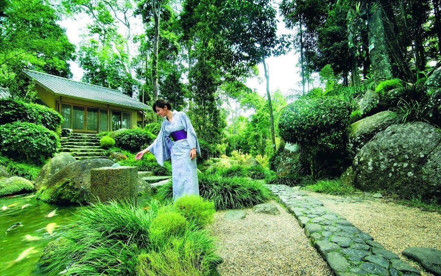 A person in traditional attire walking along a stone path in a lush garden with a pond and stepping stones. 2