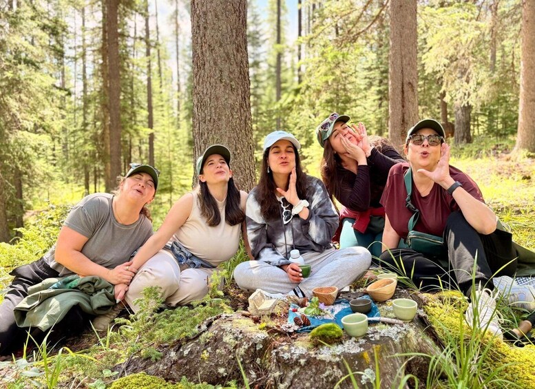 A group of people sitting on a rock in a forest with trees and greenery around. 1
