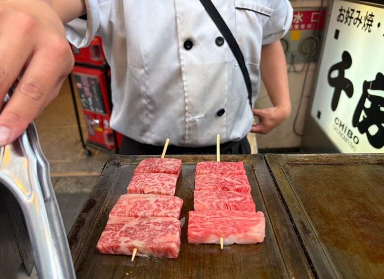 Henkilö grillaa ohuiksi viipaloituja lihapaloja puisen leikkuulaudan päällä. 1