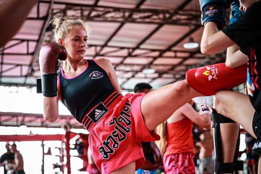 A person in a black tank top and red shorts, wearing boxing gloves, in a gym with other people in the background. 5
