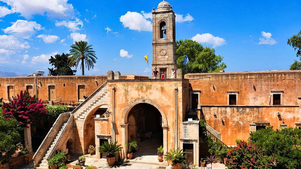 A historic building with a bell tower, arched entrance, and surrounding greenery. 1
