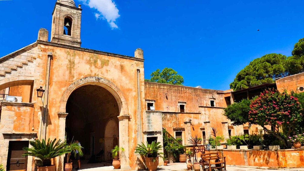 A historic building with a bell tower, arched entrance, and surrounding potted plants. 2