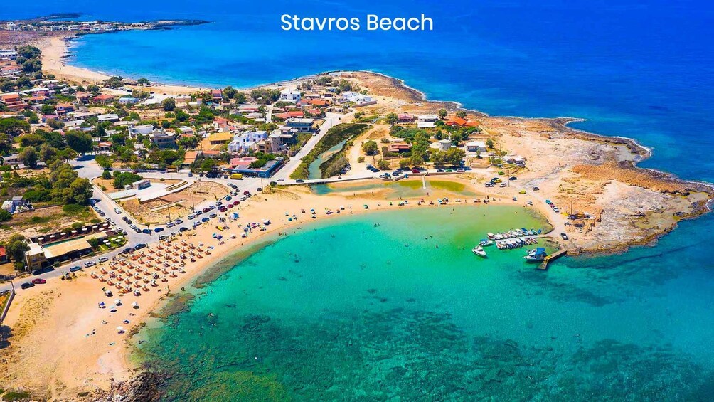 An aerial view of Stavros Beach with clear turquoise waters, a sandy beach, and surrounding residential buildings. 3