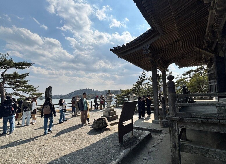 A traditional Japanese temple with visitors, a stone lantern, and a view of the water. 5