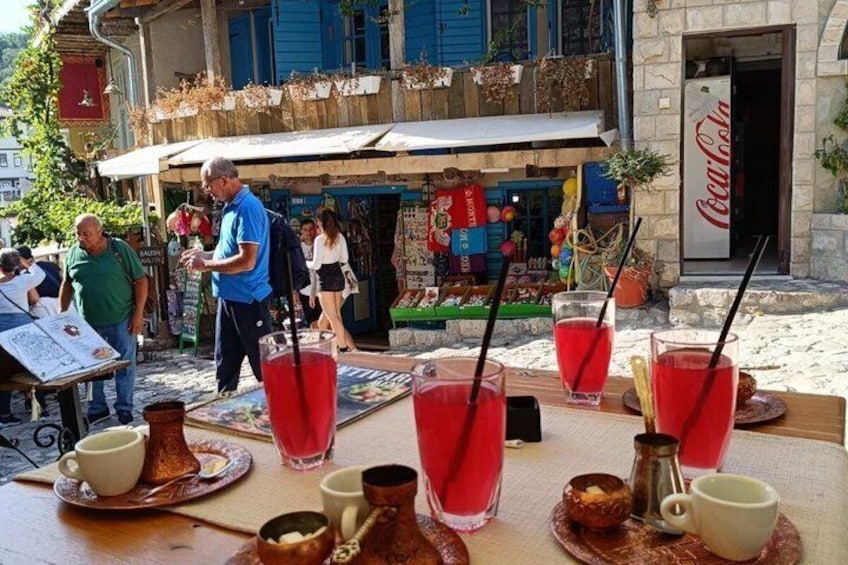 A table with red drinks and coffee cups, a Coca-Cola sign, and a bustling outdoor market. 3