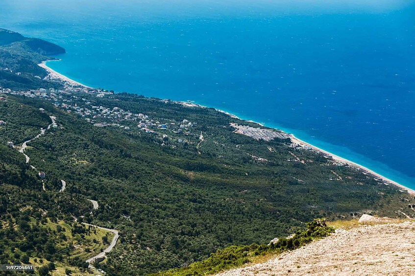 A coastal landscape with a winding road, dense greenery, and a beach. 2