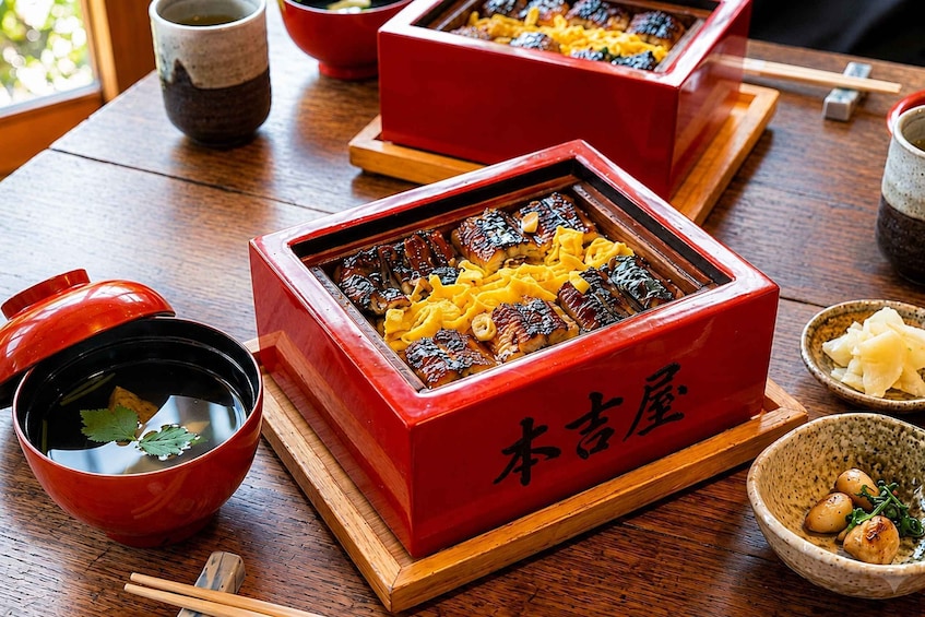 A traditional Japanese meal with a red lacquered box containing grilled fish and vegetables, accompanied by a bowl of soup and other dishes. 4
