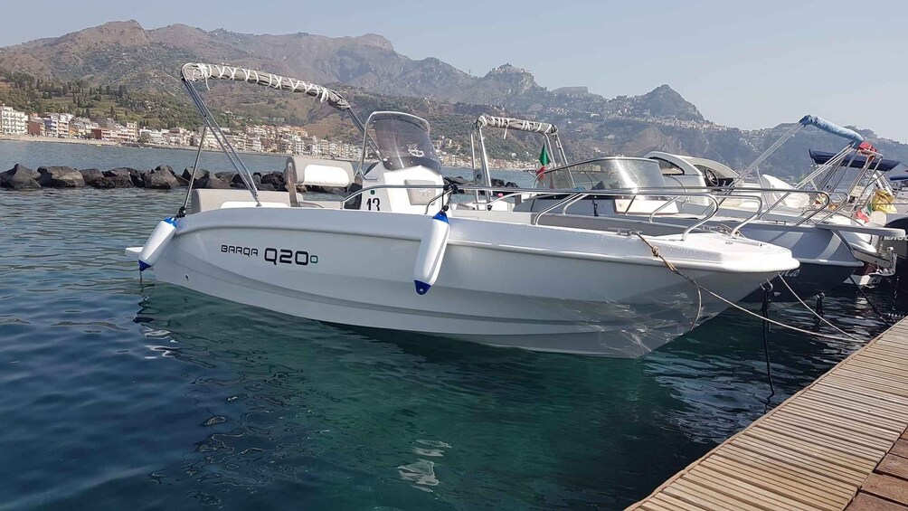 A white boat named 'GARQA Q20' docked at a marina with mountains in the background. 3