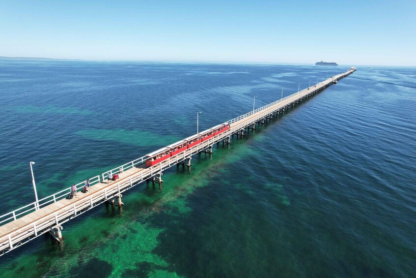 A long pier extending into the ocean with clear water and a ship in the distance. 5