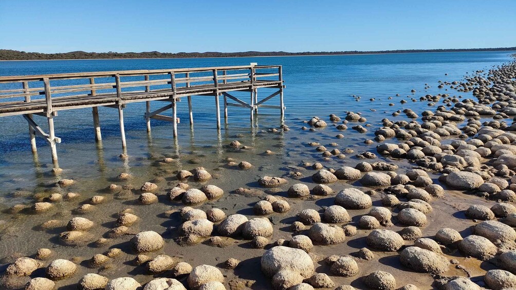 A wooden pier extending into calm waters, surrounded by numerous rounded rocks. 1