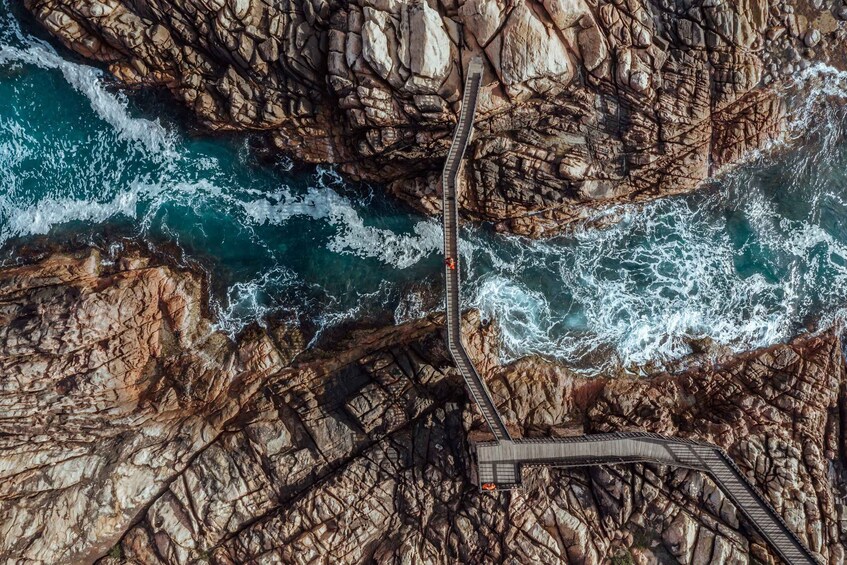An aerial view of a coastal area with rocky cliffs, a winding road, and a small bridge. 2