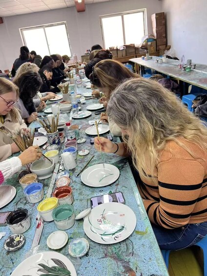 A group of people engaged in pottery making, with various bowls and paint containers on a table. 5