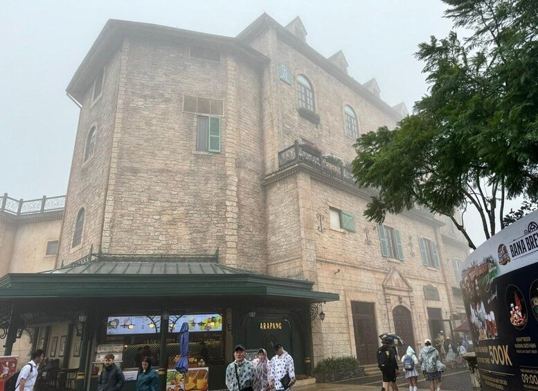 A historic stone building with a green awning, a sign reading 'ARAPANG,' and a crowd of people in the foreground. 2