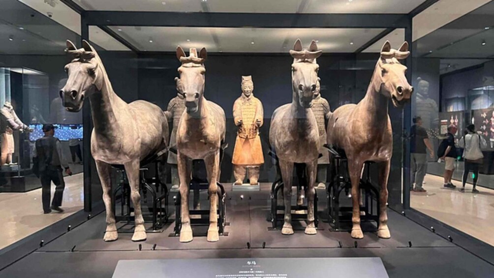 A museum exhibit featuring four horse statues and a human figure in the center. 4