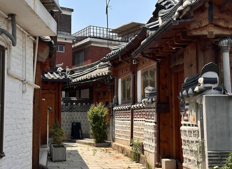 A traditional Korean alleyway with wooden buildings, tiled roofs, and a small tree. 2