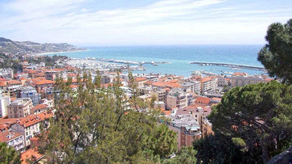 A coastal cityscape with dense urban buildings, a marina with boats, and a clear blue sea. 3