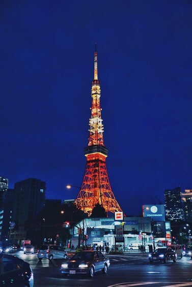 A brightly lit tower resembling the Eiffel Tower at night, surrounded by city buildings and busy traffic. 1