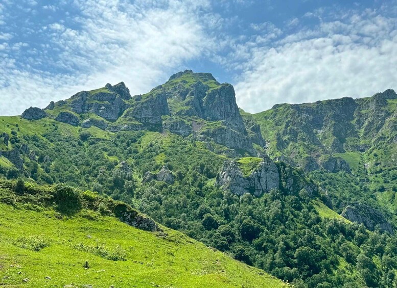 A mountainous landscape with lush green hills and rocky peaks under a partly cloudy sky. 5