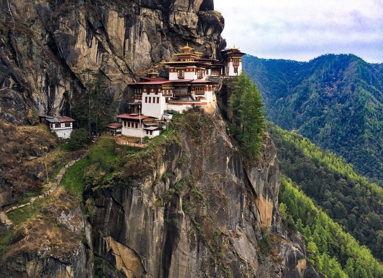 A monastery perched on a cliffside with a forested valley below. 1
