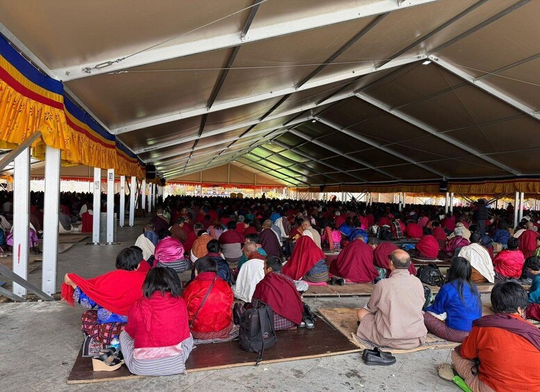 A group of people seated in a tented area, some wearing traditional attire. 2