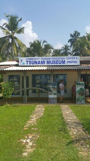 A building labeled 'Community Tsunami Education Center & Tsunami Museum (Photos)' with palm trees and a clear sky in the background. 5