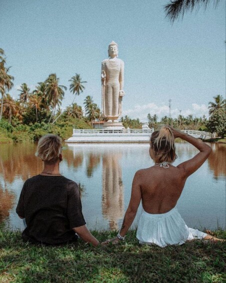 Two people sitting by a lake, facing a large Buddha statue. 4