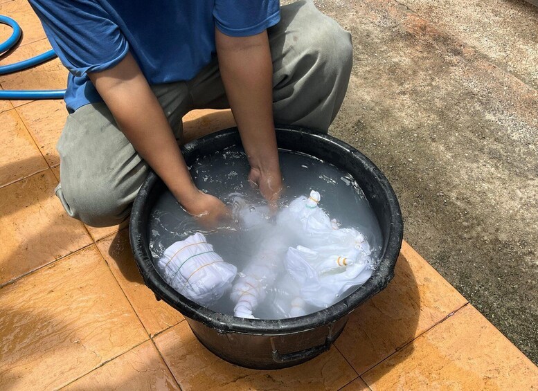 A person kneeling beside a large black bucket filled with water and plastic bottles. 3