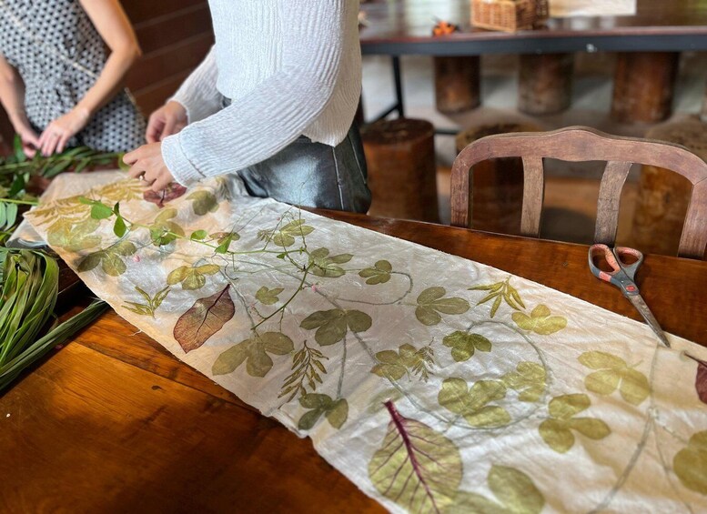 A table with a tablecloth featuring a leaf pattern, a pair of scissors, and a wooden chair. 1