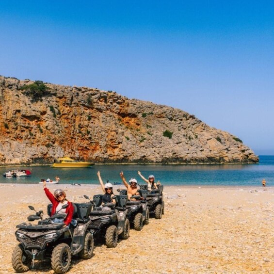 A group of people on ATVs on a pebble beach with a rocky cliff and calm sea in the background. 5