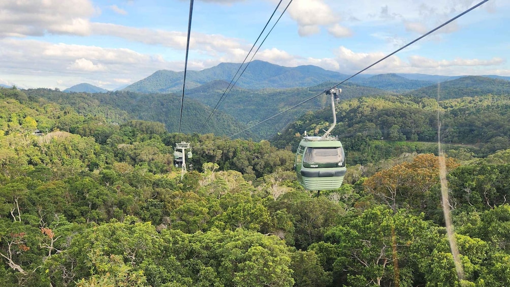 A cable car suspended over a dense forest with mountains in the background. 3