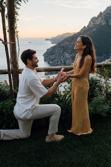 A man proposing to a woman by the seaside with a mountainous backdrop. 4