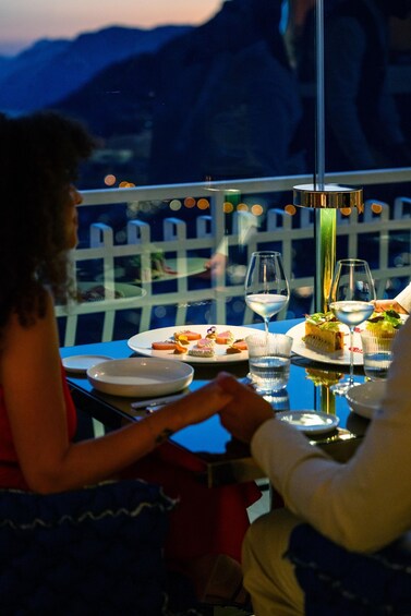 A couple dining at a table with a mountain view, plates of food, and wine glasses. 5