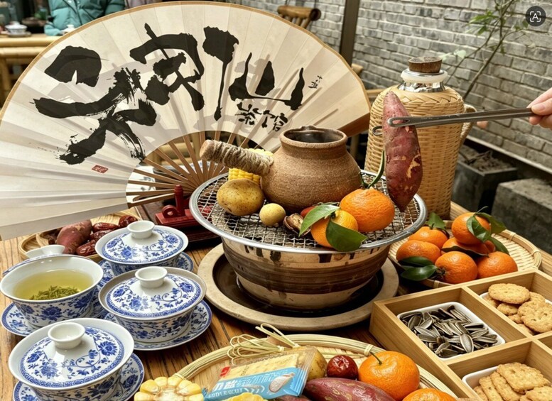 A traditional Chinese tea set, a fan with calligraphy, a grill with food, and various snacks. 2