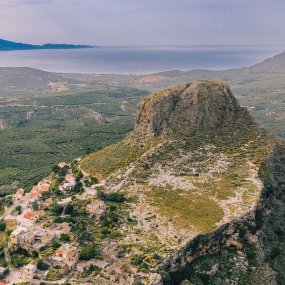 A coastal village nestled in a valley with terraced fields and a prominent rocky hill. 3