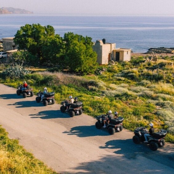 A group of people riding ATVs on a dirt road with a coastal landscape in the background. 4