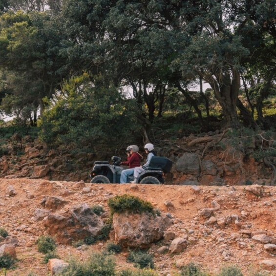Two people on a quad bike in a rocky terrain with trees in the background. 5