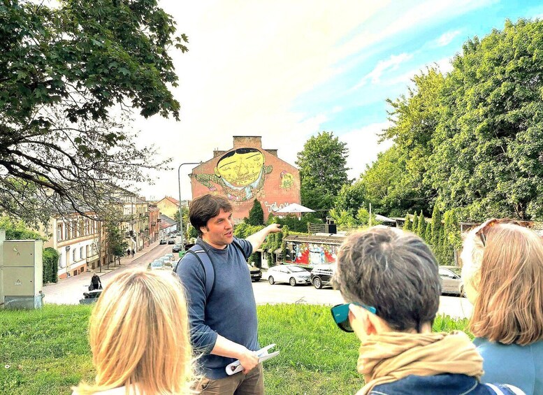A person pointing at a mural on a building, with a street and parked cars in the background. 4