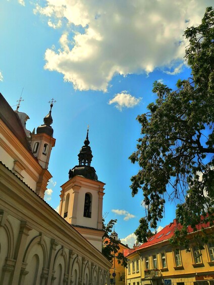 A church with a bell tower and a red-tiled roof, surrounded by buildings and trees. 3