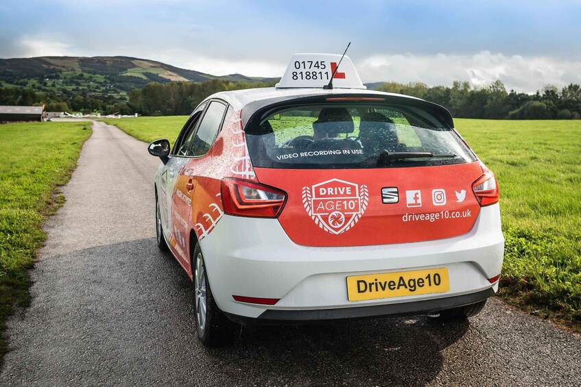 A white car with red accents and a license plate 'DriveAge10' parked on a rural road. 3