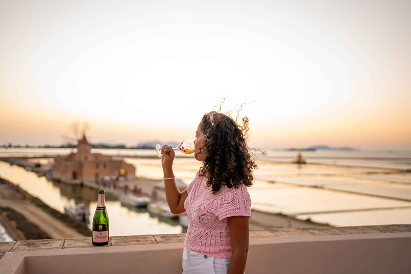 A person drinking a beverage with a bottle labeled 'Lancer' on a balcony overlooking a waterfront with buildings in the background. 1