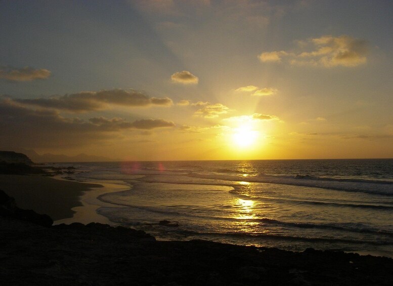 A sunset over a beach with waves reflecting the sun. 2