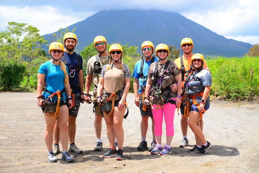 A group of people with helmets and harnesses, standing on a dirt path with a mountain in the background. 2