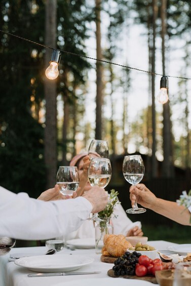 A group of people toasting with wine glasses at an outdoor table with a forest backdrop. 5