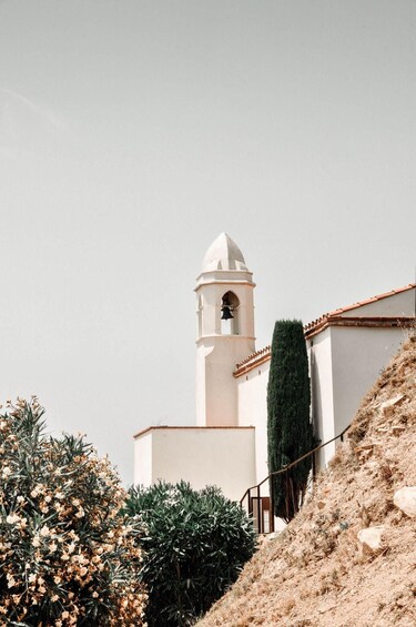 A white church with a bell tower, surrounded by dry shrubs and a tall green hedge. 1