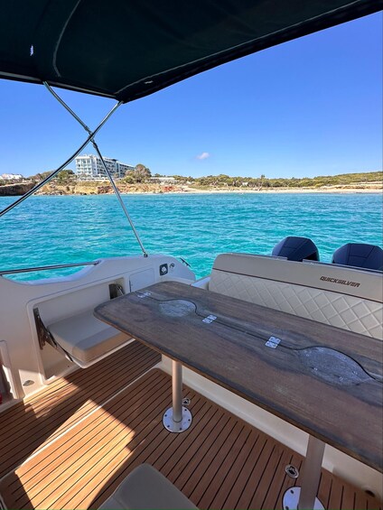 A boat deck with a wooden table, cushioned seating, and a view of a coastal landscape with buildings and a beach. 2