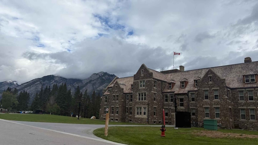 A stone building with a Canadian flag, surrounded by mountains and trees. 3