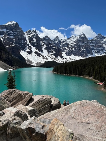 A mountain lake with clear turquoise water, surrounded by snow-capped peaks and dense forest. 1